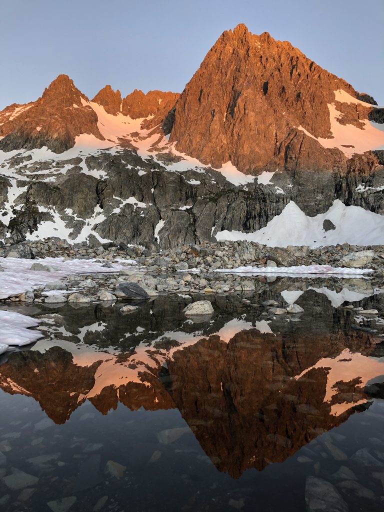 A photo of mountains a-glow from the sunset, reflecting in a pool of water