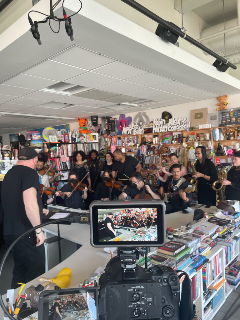 musicians performing during the tiny desk filming with a camera in the foreground