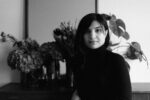 Portrait of a woman in a black turtleneck indoors, with leafy plants in the background.